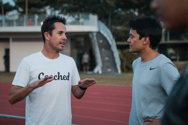 A coach and runner engaged in a conversation on a running track