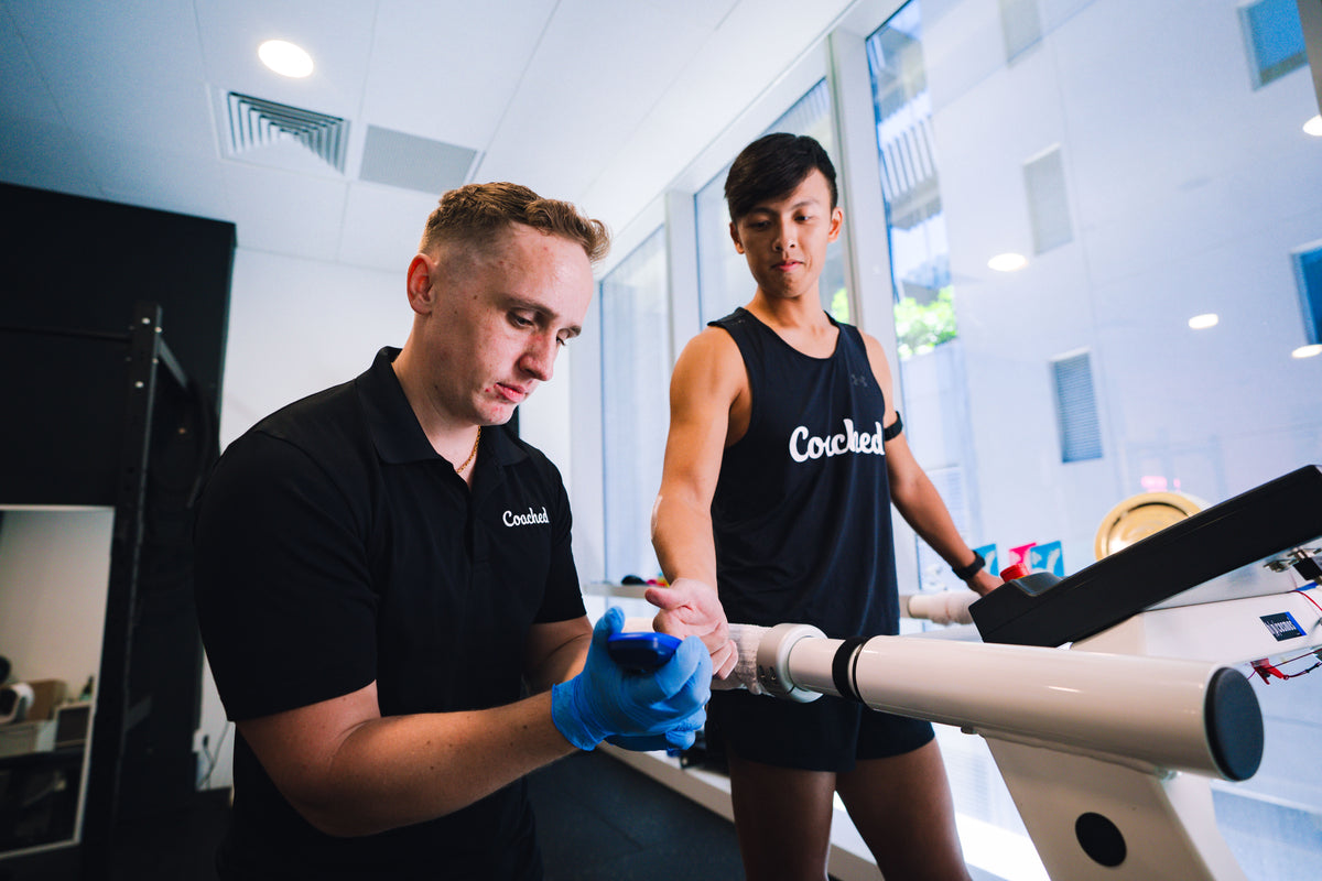 An exercise physiologist collects a blood sample from a runner standing on a treadmill